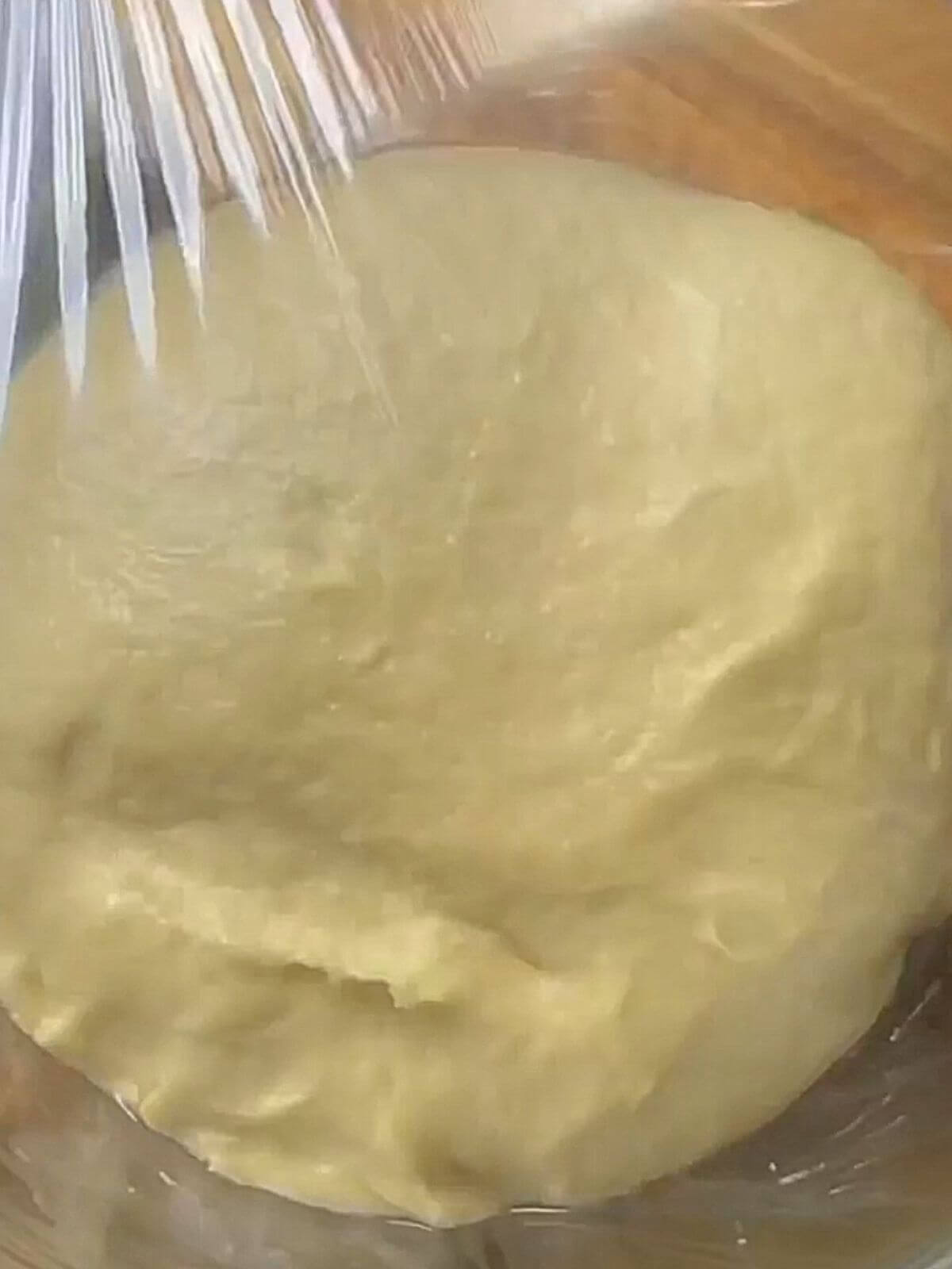 Dough in a glass bowl covered with cling film, resting to rise and double in size.