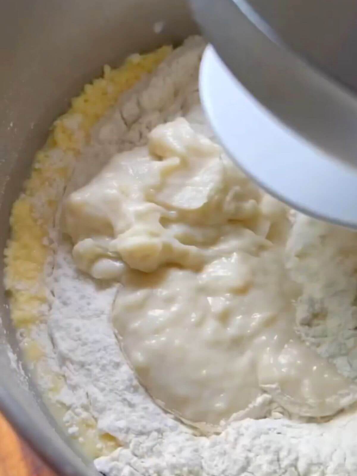 Ingredients for soft buns dough in a mixing bowl, including milk, bread flour, yeast, sugar, salt, butter, egg, and tangzhong mixture, ready to be mixed.