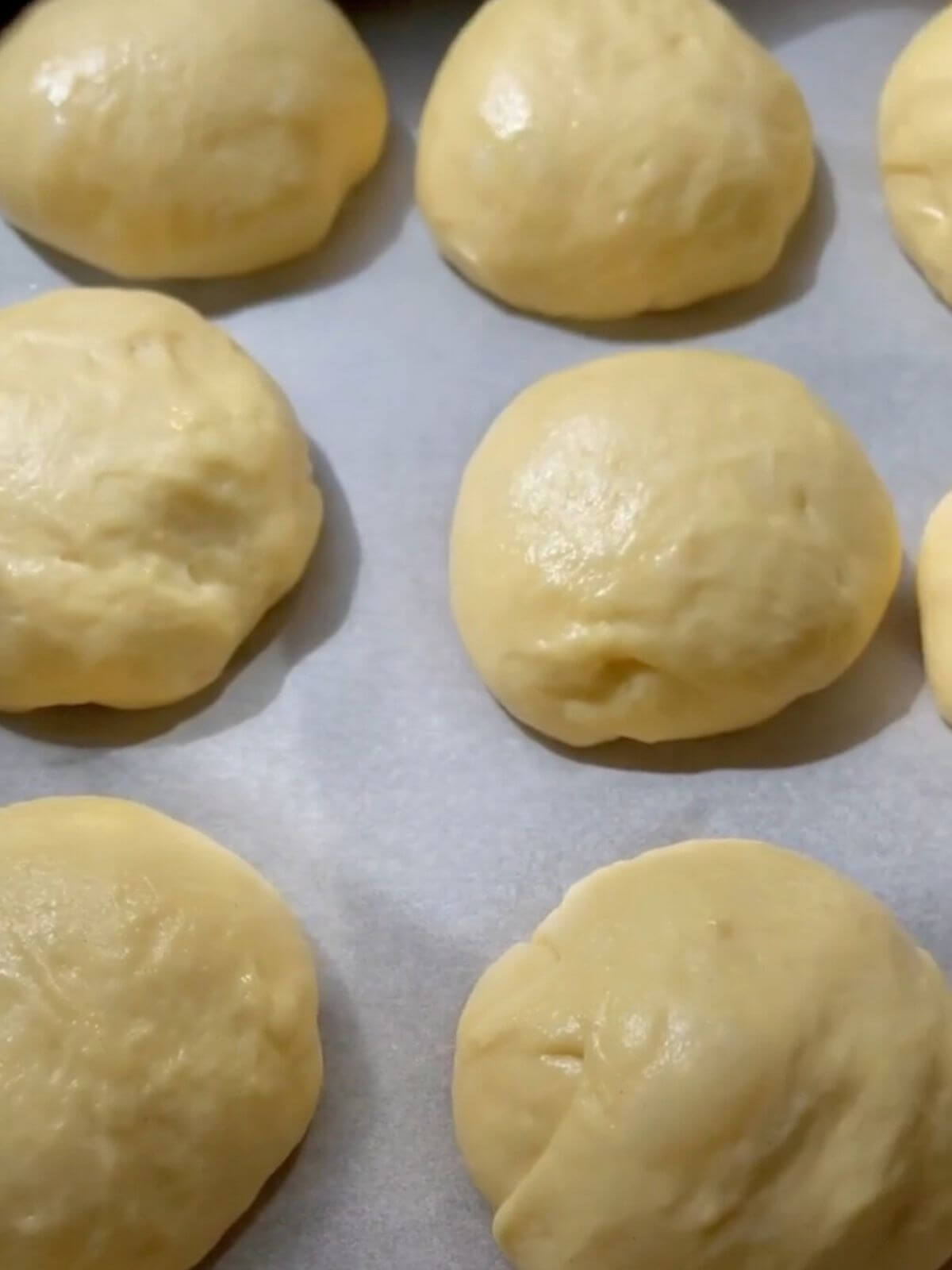 Dough shaped into balls, placed on a baking tray, ready to rise and become soft burger buns.