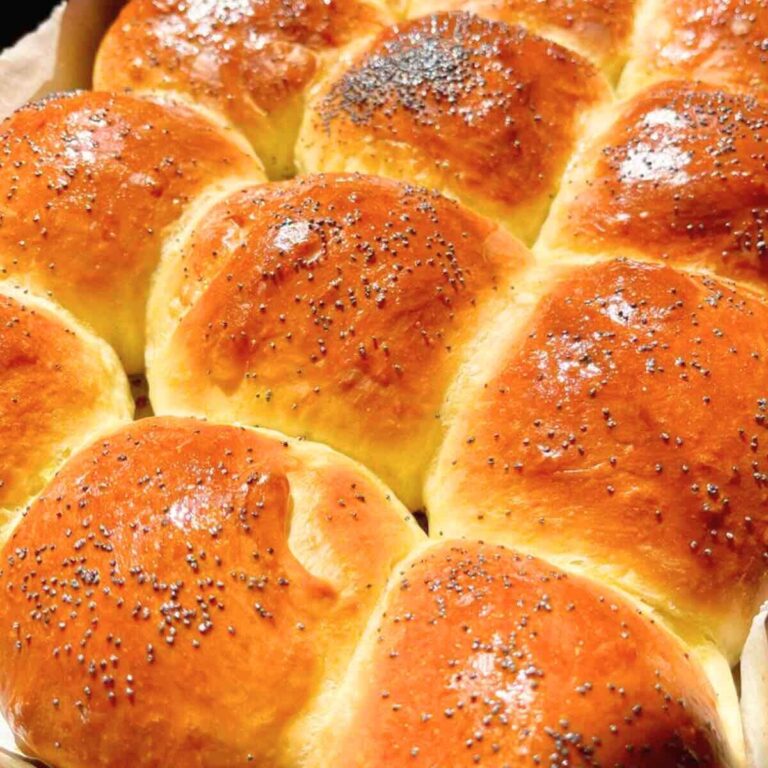 Freshly baked golden brown burger buns cooling in a pan.