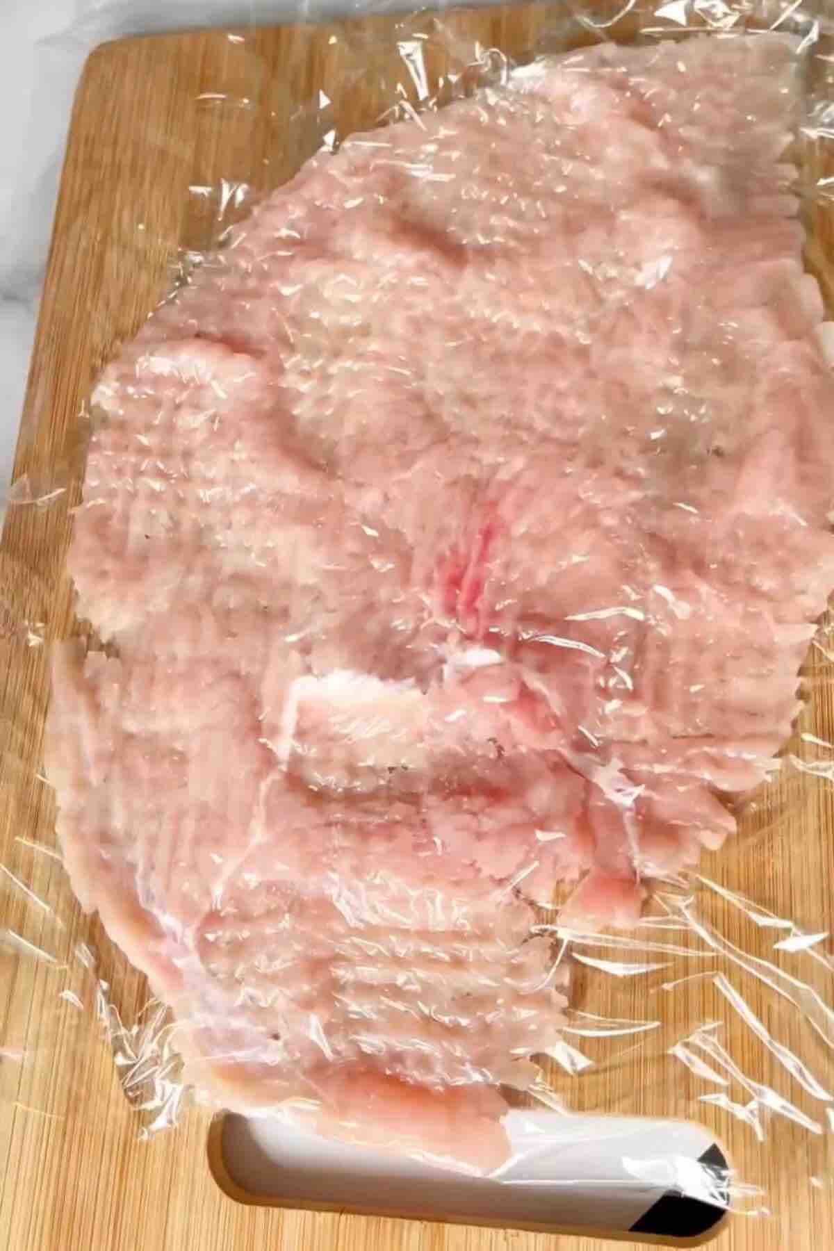 A tenderized piece of chicken breast, flattened and ready for cooking.