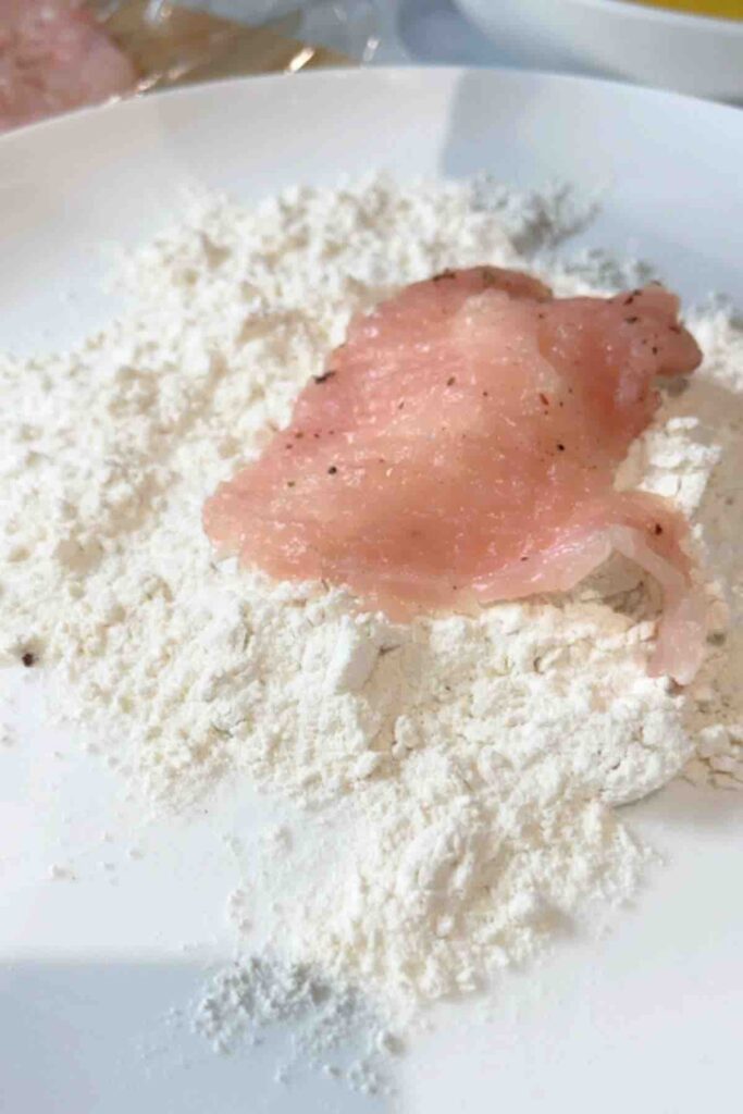 A piece of chicken breast that has been tenderized and is ready to be coated with flour.