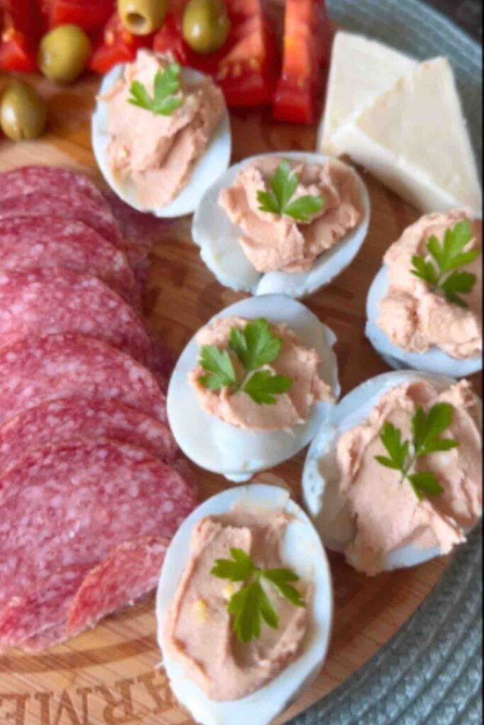 Deviled Eggs on a wooden board with salami, tomatoes and green olives