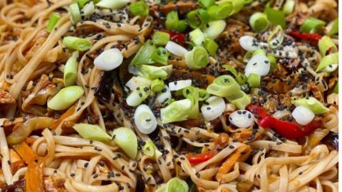 Chicken noodles in a pan, topped with fresh green onions and sesame seeds