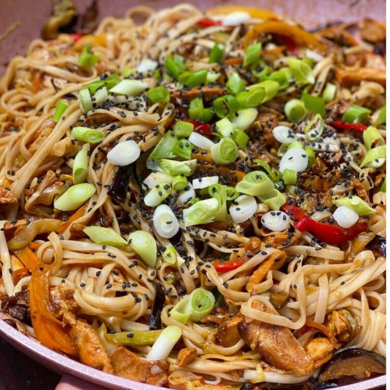 Chicken noodles in a pan, topped with fresh green onions and sesame seeds