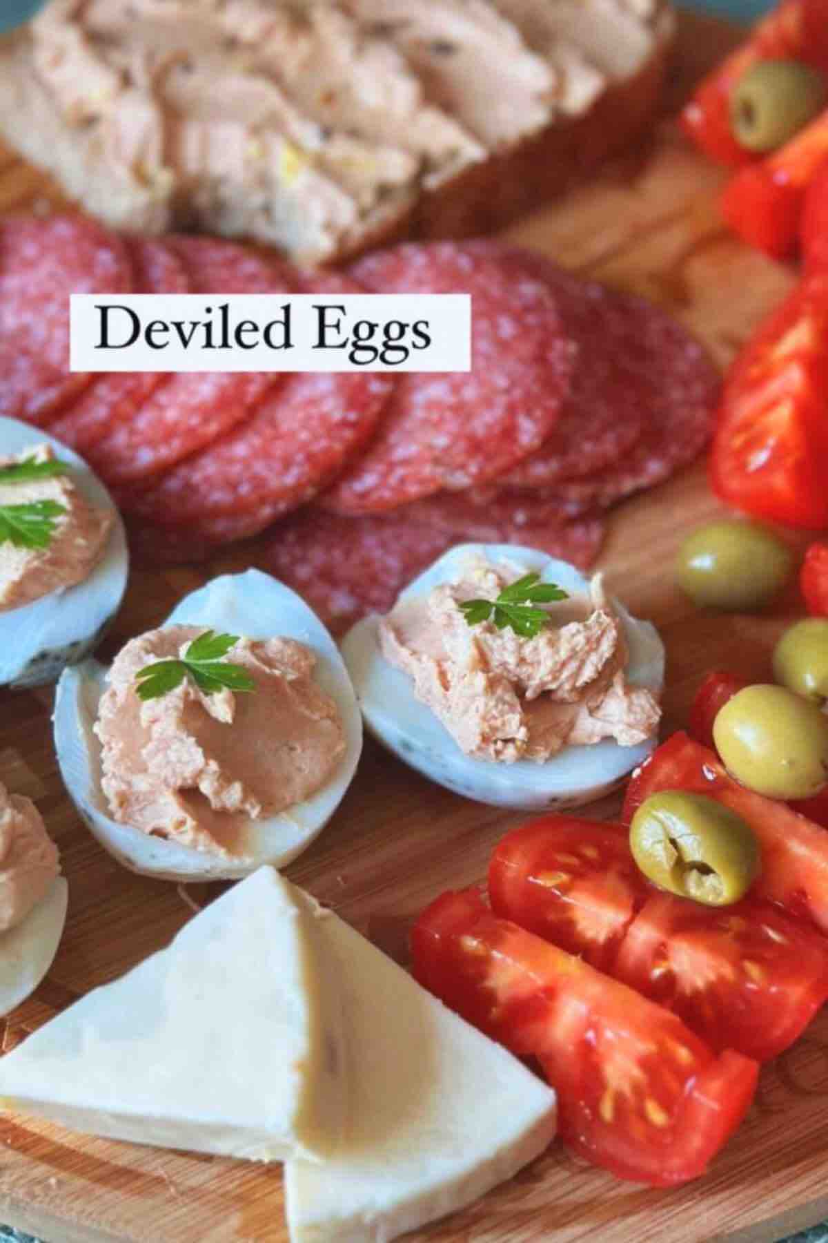 Deviled Eggs on a wooden board with salami, tomatoes, soft cheese triangles and green olives