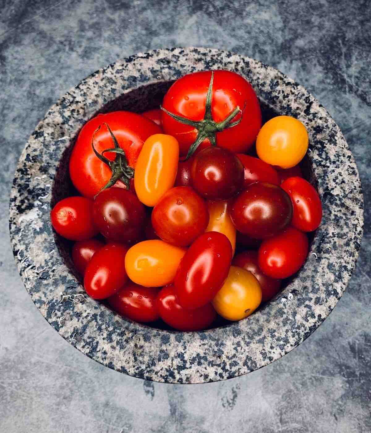 Multicolored large and cherry tomatoes displayed in a mortar, showcasing their vibrant hues and fresh appearance.