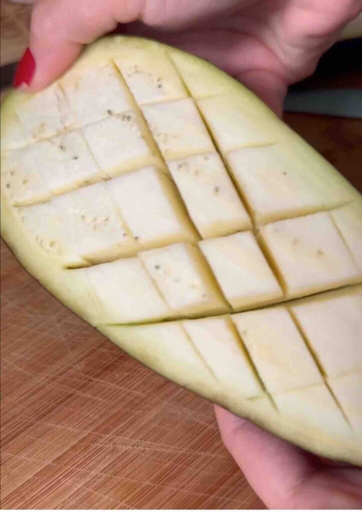 Half of an aubergine, crosswise scored, prepared for baking.