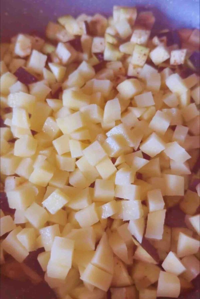 Olive oil in a pan with cubed potatoes and eggplant, ready to be sautéed.