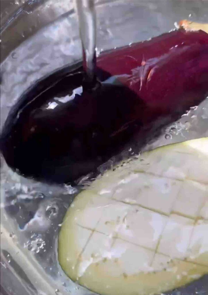 Two halves of aubergine, crosswise scored and soaking in water to remove bitterness.