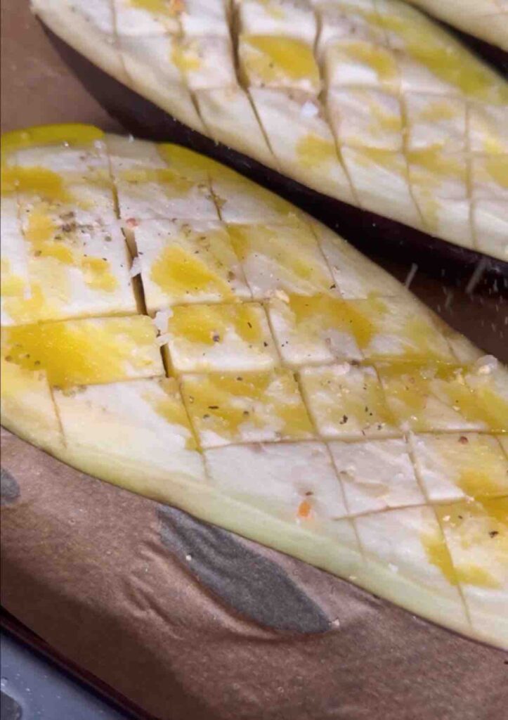 Two aubergines cut in half, scored crosswise, sprinkled with olive oil and salt, and placed on a tray ready for baking.