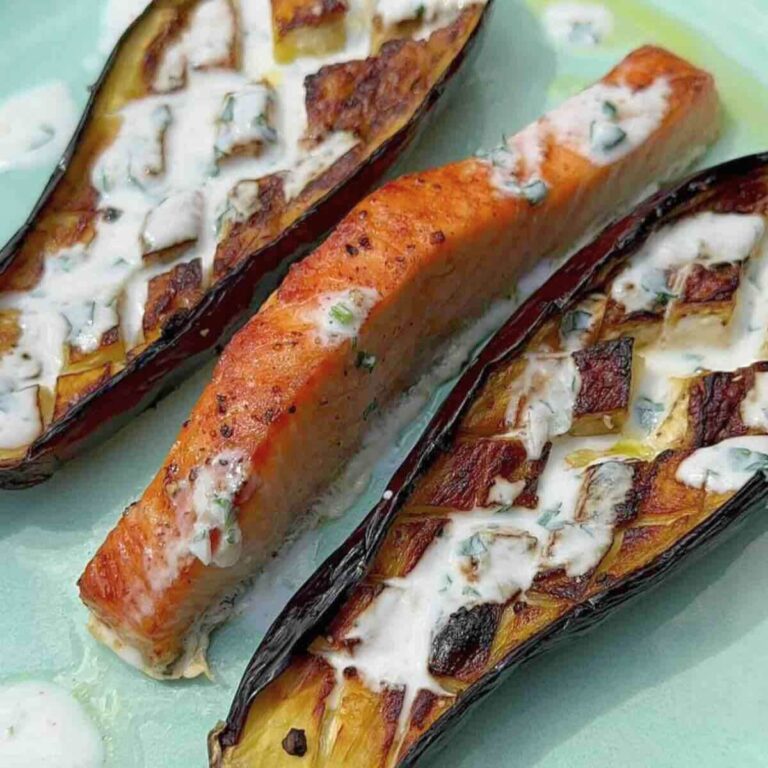 A plate with baked aubergine and salmon with a drizzle of yoghurt dressing.