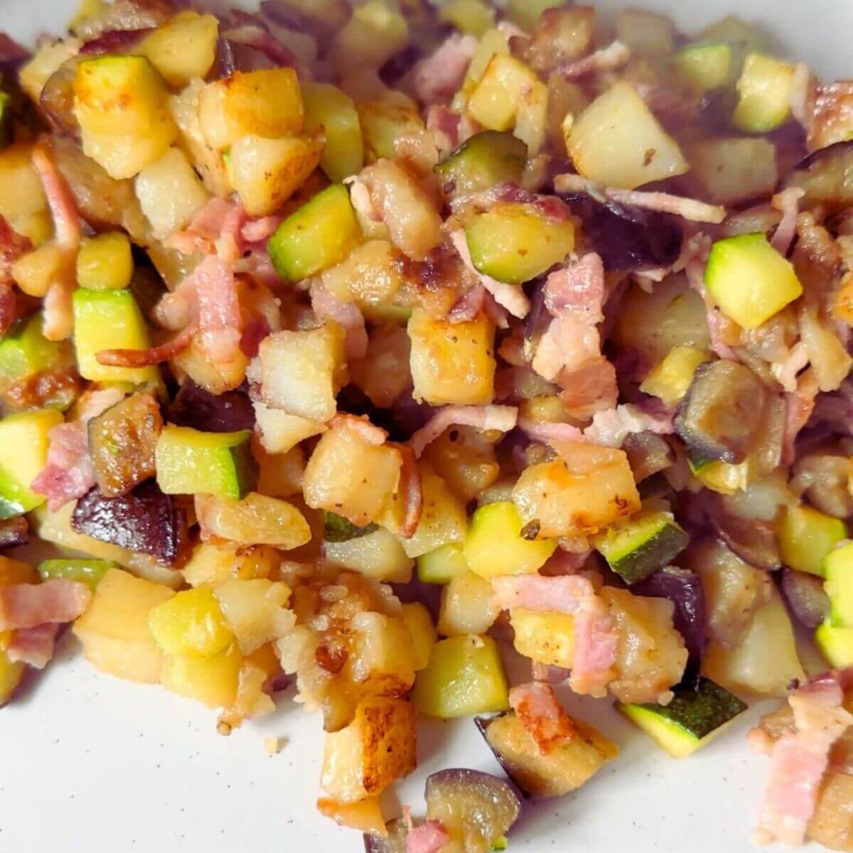 Plate of sizzling bacon, tender potatoes, and sautéed zucchini hash.