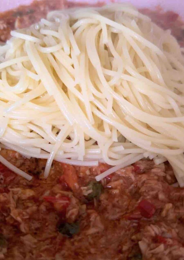 Pan with tuna in olive oil, garlic, chili, and capers in tomato sauce, with cooked spaghetti being added.