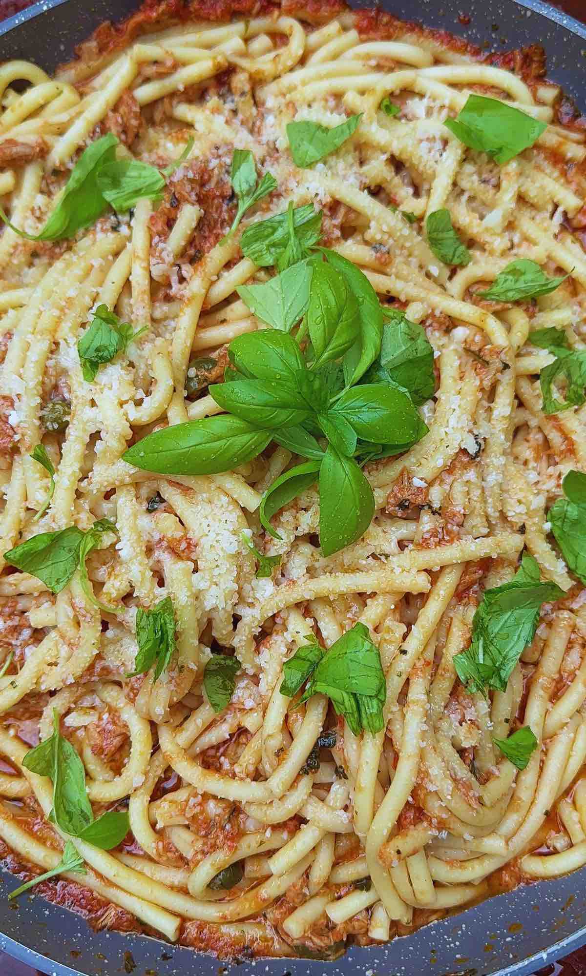 Tuna, caper & chilli bucatini in a large pan garnished with fresh basil