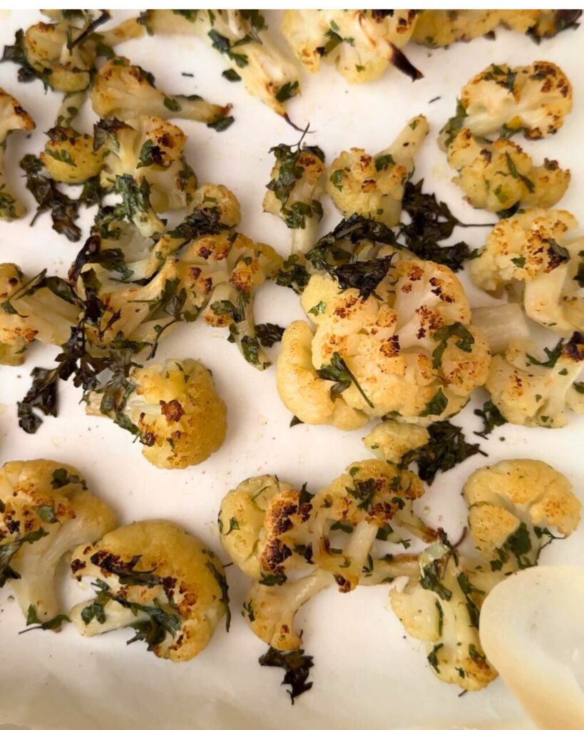 Roast cauliflower florets drizzled with 4 tablespoons of olive oil, seasoned with salt and pepper, and garnished with a small bunch of parsley, arranged in a parchment-lined pan, freshly baked and ready to serve.