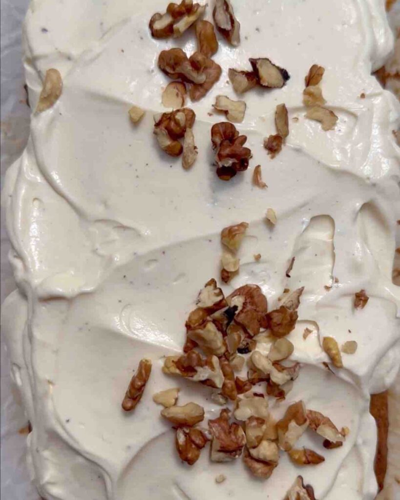 Vegan carrot cake banana bread topped with cream cheese frosting and walnuts.