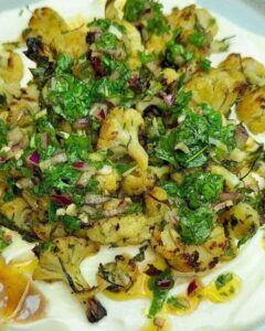 Roasted cauliflower on a plate with a creamy yogurt base, generously topped with vibrant chimichurri sauce, showcasing a colorful and appetizing dish.