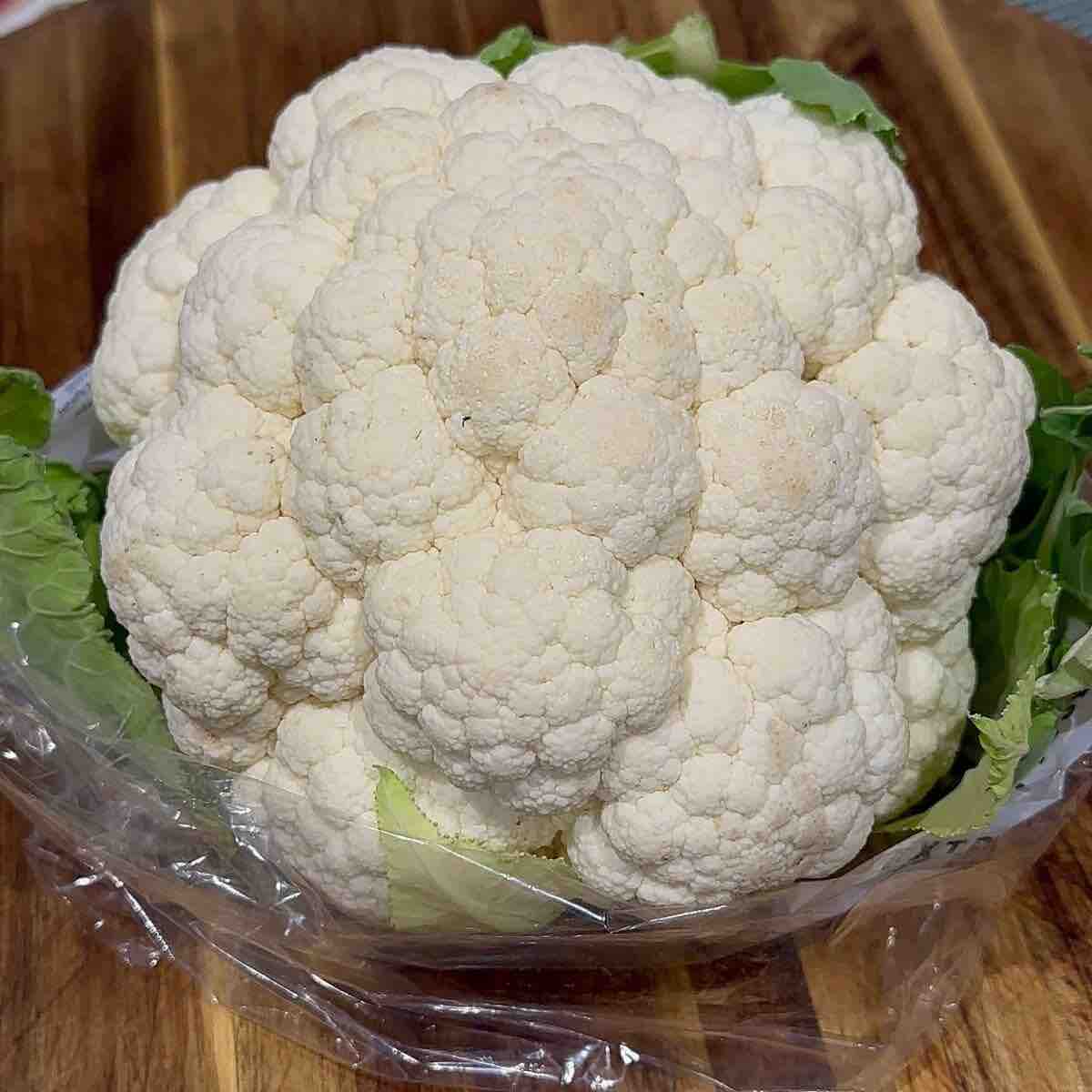 A head of white cauliflower displayed on a rustic wooden board, highlighting its fresh and natural appearance.