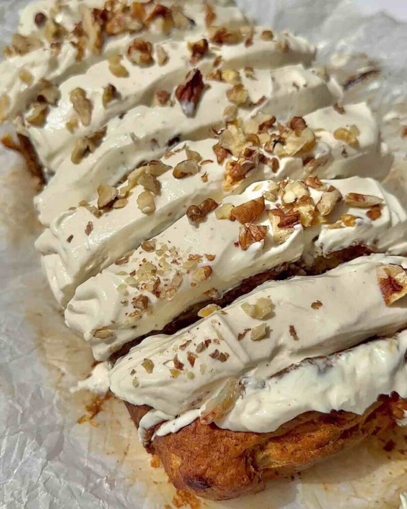 Vegan carrot cake banana bread topped with cream cheese frosting and walnuts.