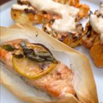 Salmon fillets marinated and baked with lemon slices and fresh basil atop, enveloped in parchment paper, accompanied by cauliflower steaks.