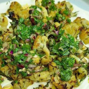 Roasted cauliflower on yogurt sauce, topped with green herb sauce, served on a plate.