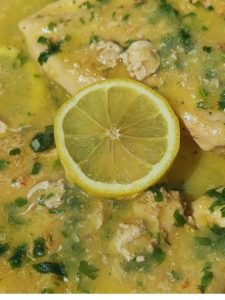 Two succulent lemon-infused chicken breast fillets with a zesty lemon sauce, garnished with fresh lemon slices and vibrant green herbs, beautifully presented in a pan.