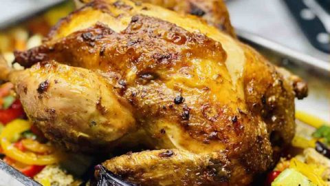 A photo showing a roast chicken in a baking tray with roasted veggies all around.