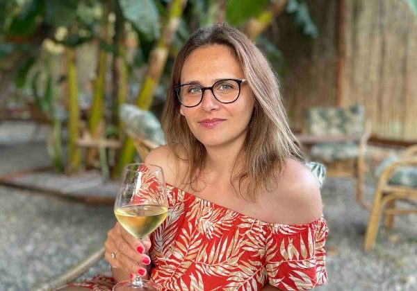 A photo showing the creator of this food blog holding a glass of white wine. 