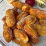 A bowl of golden brown apple doughnuts generously coated with a delightful mix of cinnamon and sugar.