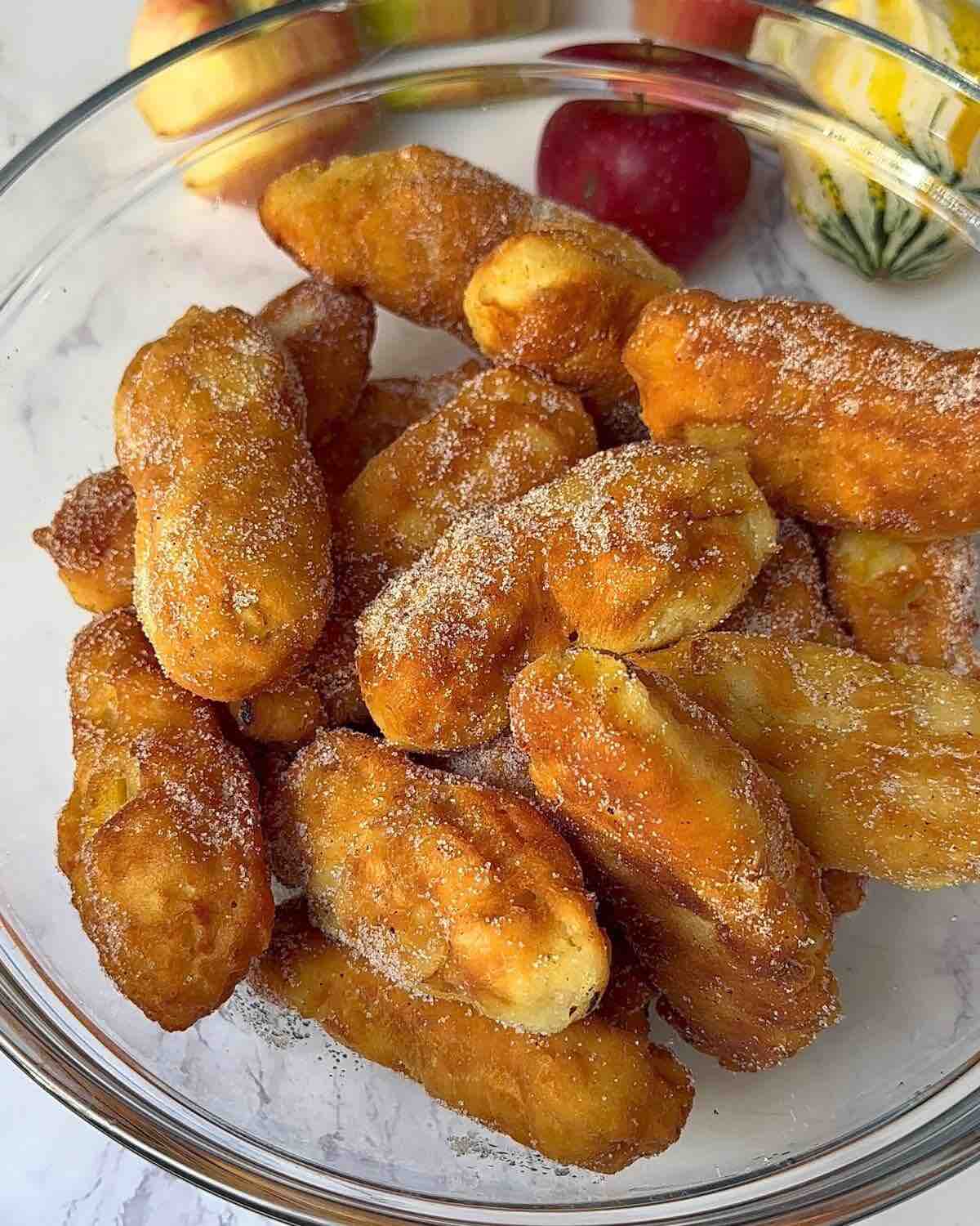 A bowl of golden brown apple doughnuts generously coated with a delightful mix of cinnamon and sugar.