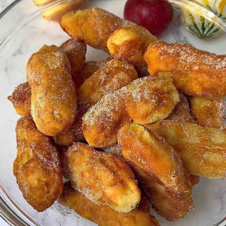 A bowl of golden brown apple doughnuts generously coated with a delightful mix of cinnamon and sugar.