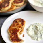 A photo showing a plate with fried potato and tuna patties served with tzatziki sauce.