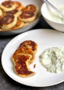 A photo showing a plate with fried potato and tuna patties served with tzatziki sauce.