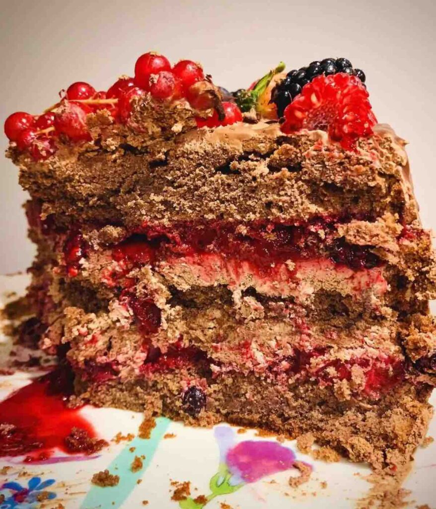 A slice of moist, rich chocolate berry mousse cake with layers of creamy mousse and fresh berries on top.