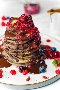 Stack of American-style Berry Pancakes drizzled with berry sauce and chocolate ganache.