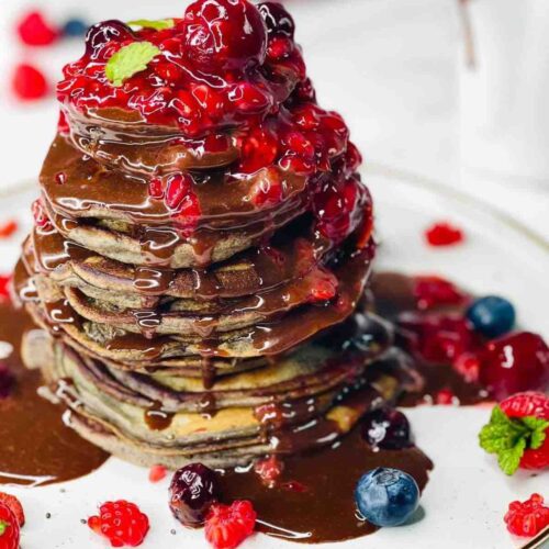 Stack of American-style Berry Pancakes drizzled with berry sauce and chocolate ganache.