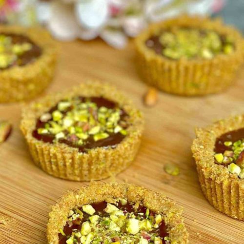 Chocolate Mini Tarts garnished with chopped pistachios on a wooden board.