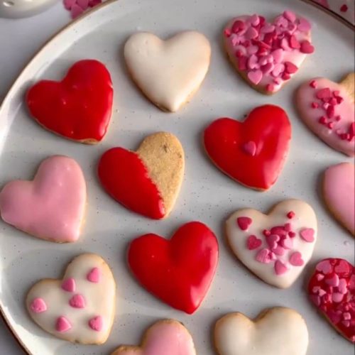 Valentine's Day iced shortbread cookies in white, red, and pink, decorated with heart-shaped sprinkles.