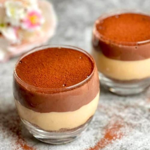 Chocolate and Caramel Pudding in two glasses, one half filled with chocolate pudding and the other half with caramel pudding, topped with cocoa powder