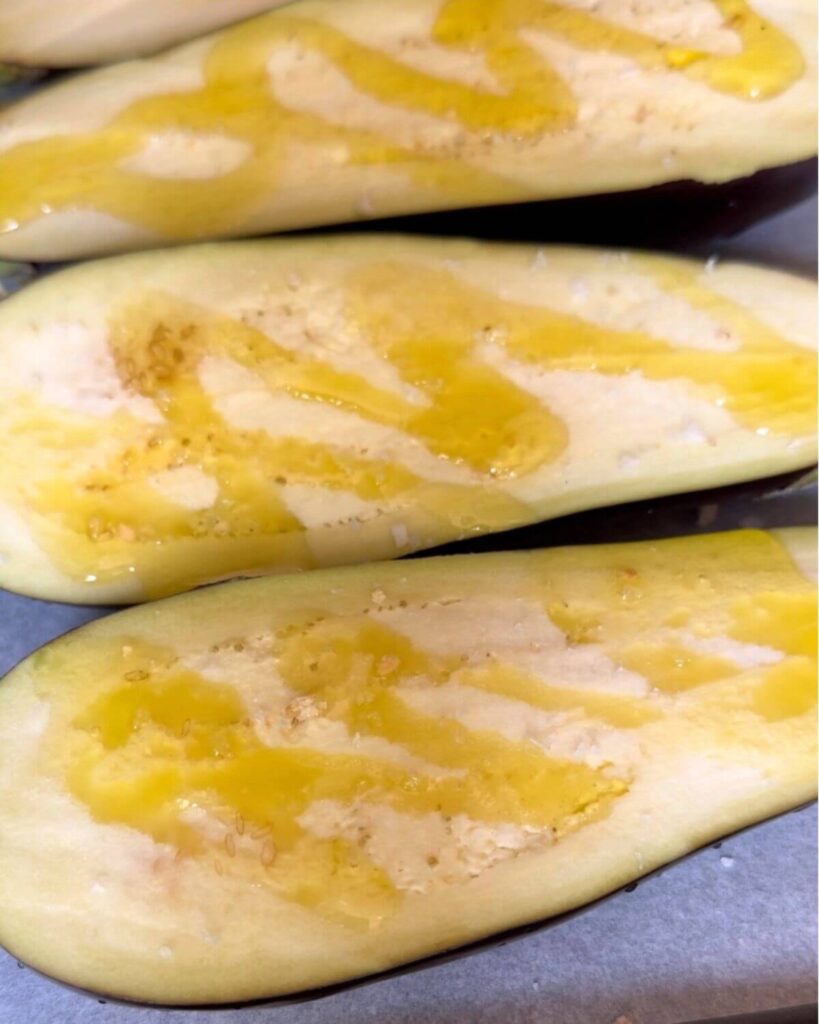 Two eggplant halves on a baking tray, drizzled with olive oil, ready to be grilled.