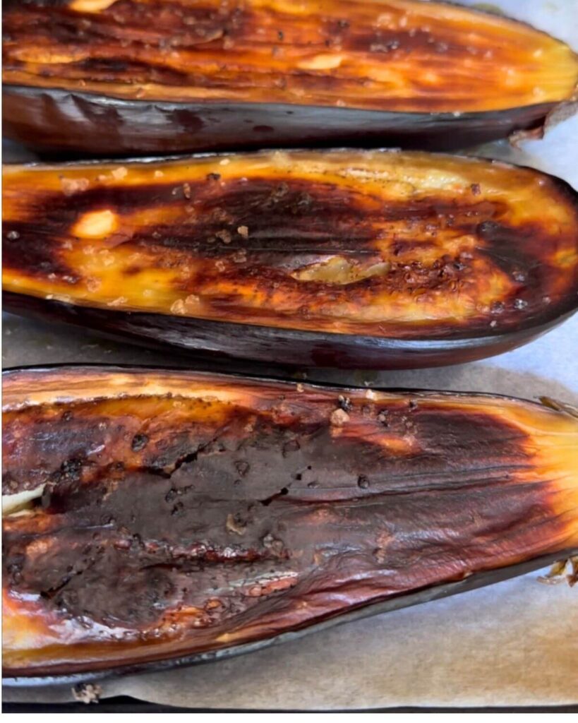 Four eggplant halves placed on a baking tray, freshly grilled.