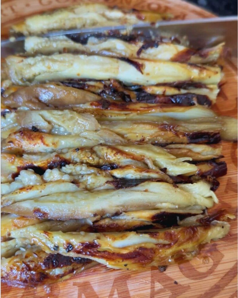 Grilled eggplant flesh on a chopping board, ready to be finely chopped for grilled eggplant salad.
