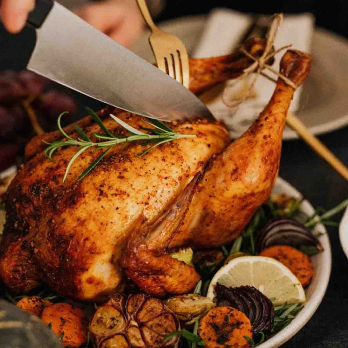 Golden roast chicken with crispy skin on a white platter, garnished with fresh herbs.