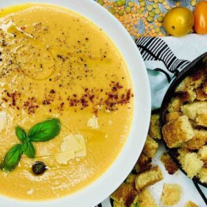 Creamy vegan lentil soup with chili powder, parmesan, basil, croutons, and dry yellow lentils in the background.