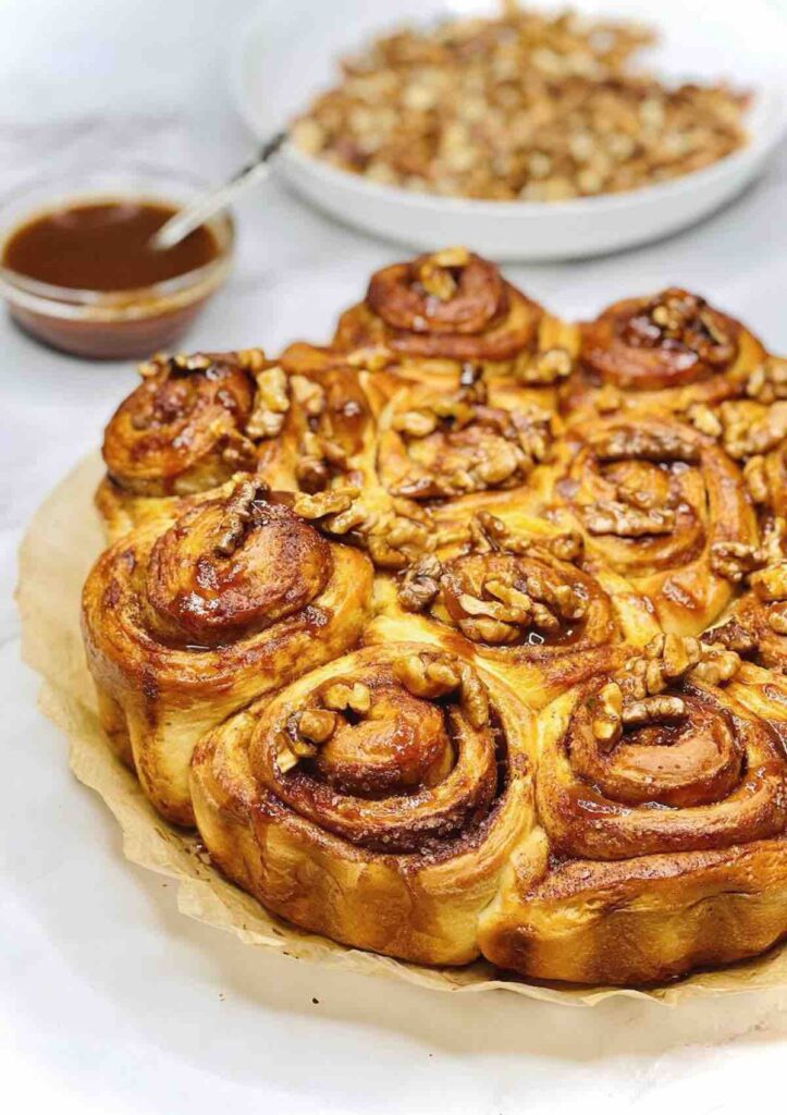 Biscoff Cinnamon Rolls with caramel sauce and walnuts in separate bowls in the background.