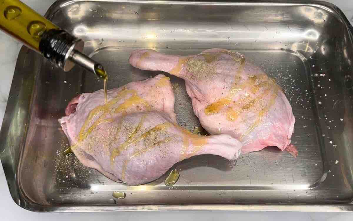 **Two duck legs seasoned with salt, pepper, and olive oil, arranged on a pan and ready to be baked.**