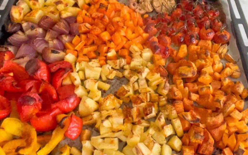 Chopped vegetables and tomatoes, with garlic, on a baking sheet, drizzled with olive oil and seasoned, baked until golden-brown.