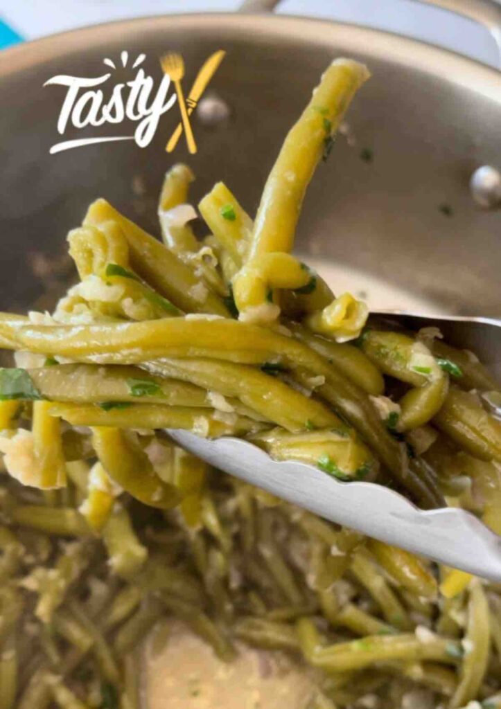 Close-up of Sautéed Green Beans with Garlic being lifted with tongs.