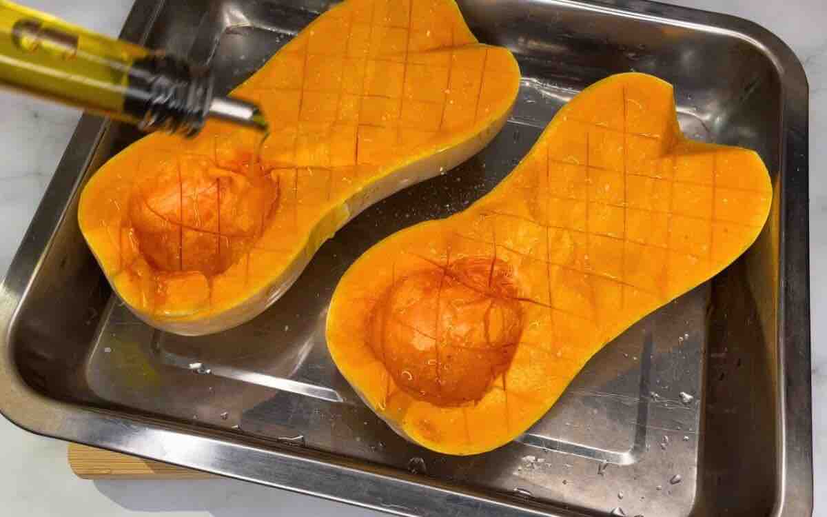 Two halves of butternut squash on a baking pan, seasoned with salt, pepper, and olive oil, ready for roasting.